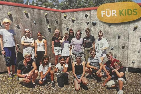 Gruppe von Kindern und Jugendlichen vor einer Kletterwand im Freien, einige lächeln in die Kamera.