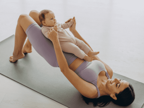 Frau in Sportkleidung macht Übungen mit Baby auf einer Yogamatte in heller Umgebung.