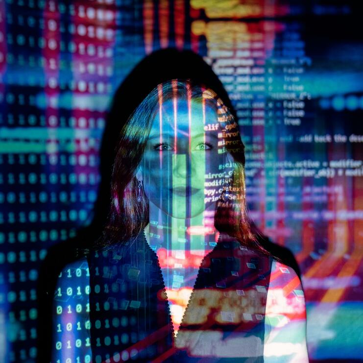 Frau mit langen Haaren, überlagert von bunten, digitalen Code-Mustern und binären Zahlen in einem dunklen Raum.