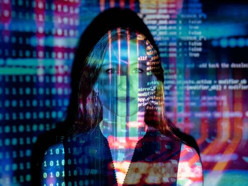 Frau mit langen Haaren, überlagert von bunten, digitalen Code-Mustern und binären Zahlen in einem dunklen Raum.
