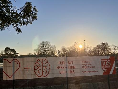 Banner mit der Aufschrift „Für + Mit Herz + Hirn Dir + Uns“ vor Sonnenuntergang im Hintergrund.