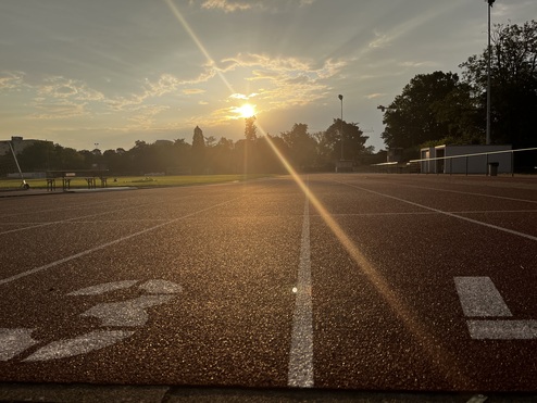 Sonnenuntergang über einer leicht feuchten Laufbahn mit Markierungen und einem Tisch im Hintergrund.