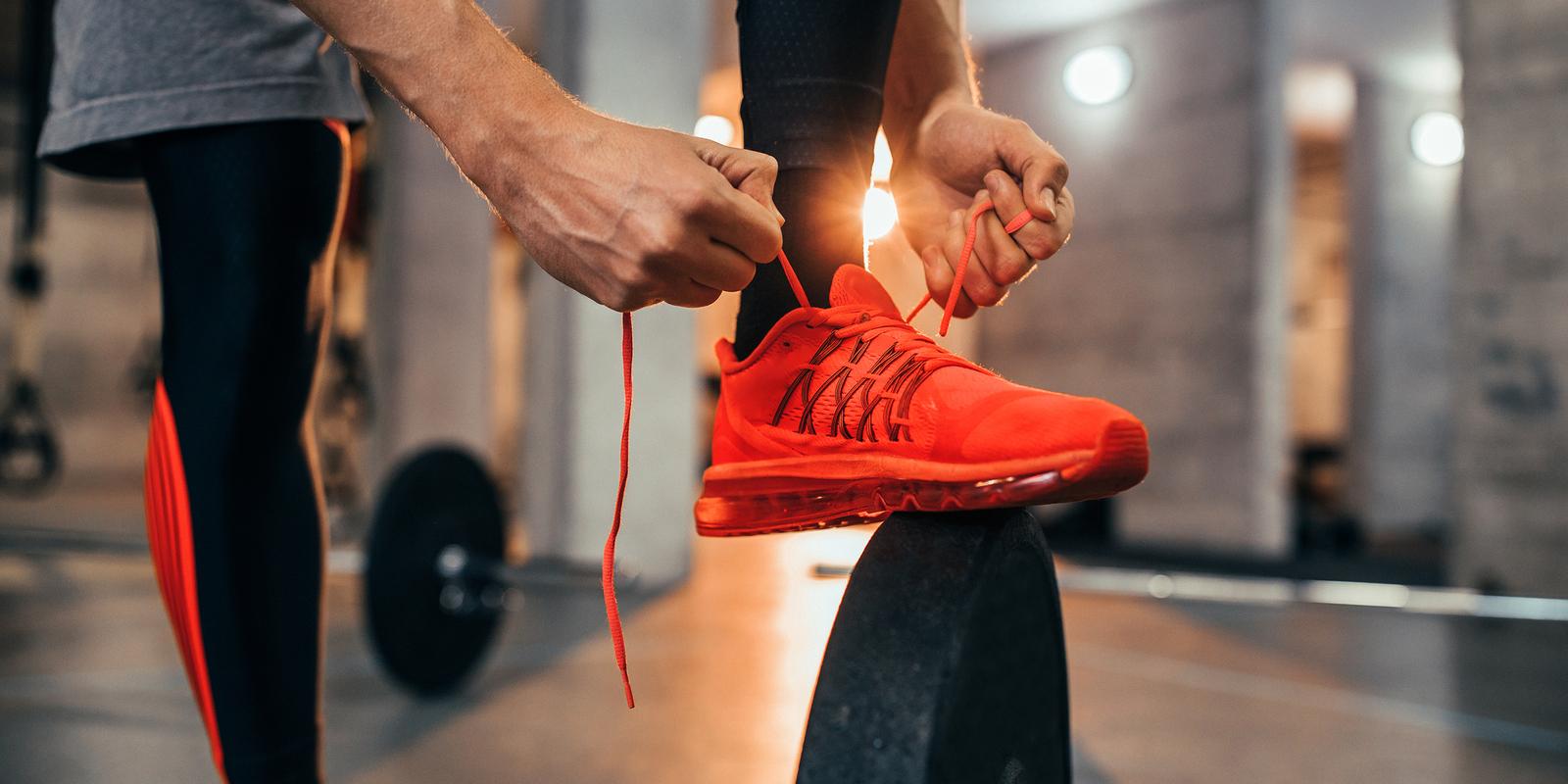 Mann bindet die Schn&uuml;rsenkel eines roten Sportschuhs auf einer Hantelplatte in einem Fitnessstudio.