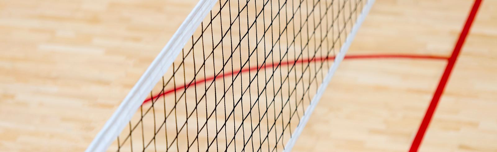 Nahaufnahme eines Badmintonnetzes auf einem Holzfu&szlig;boden mit roten Spielfeldmarkierungen.