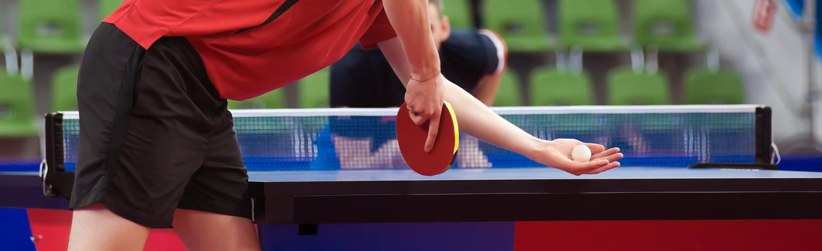 Nahaufnahme eines Tischtennisspielers in rotem Shirt, der einen Ball in der Hand h&auml;lt und sich auf den Schlag vorbereitet.