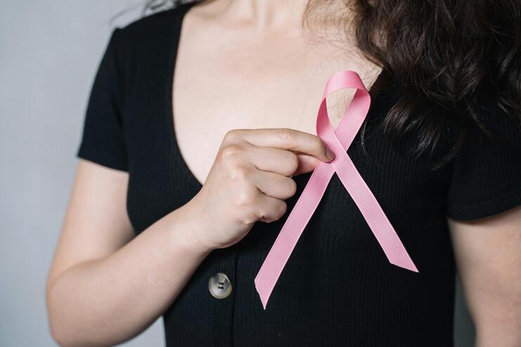 Nahaufnahme einer Person in schwarzer Kleidung, die ein rosa Bewusstseinsband mit der Hand hält.