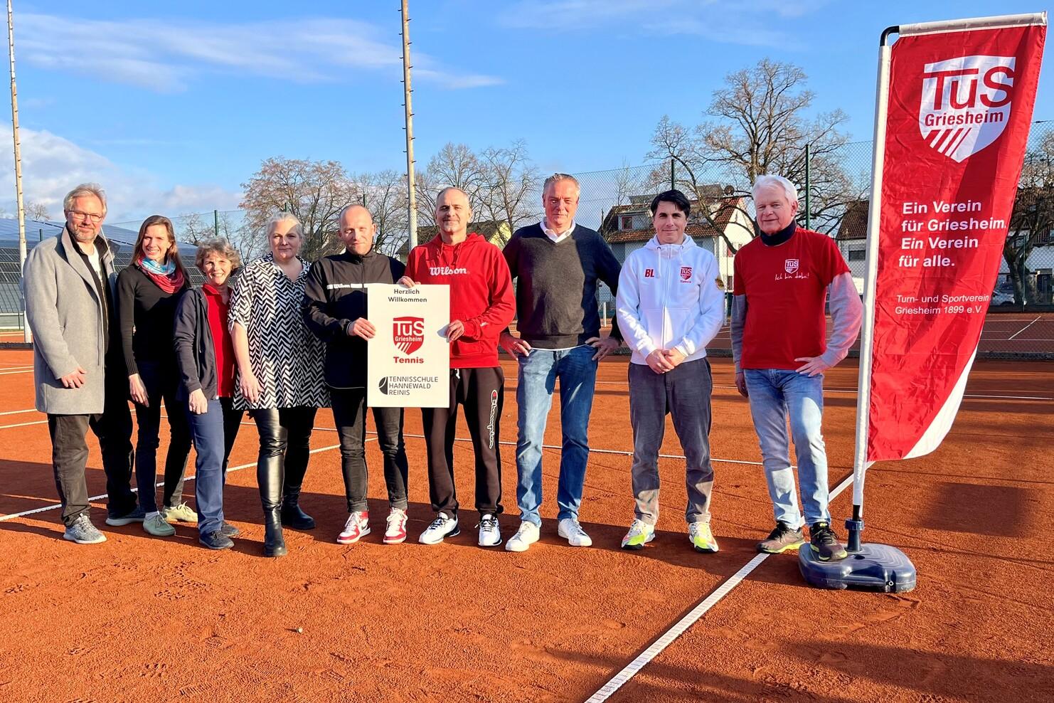 Gruppierung von neun Personen auf einem Tennisplatz, mit einem Banner des TuS Griesheim im Hintergrund.