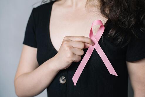 Nahaufnahme einer Person in schwarzer Kleidung, die ein rosa Bewusstseinsband mit der Hand hält.