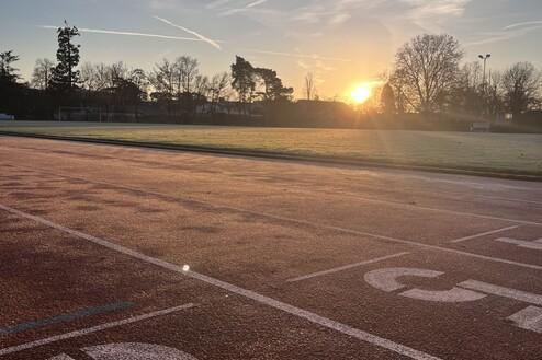 Sonnenaufgang &uuml;ber einer Laufbahn, mit Startlinien und frostbedecktem Gras im Hintergrund.