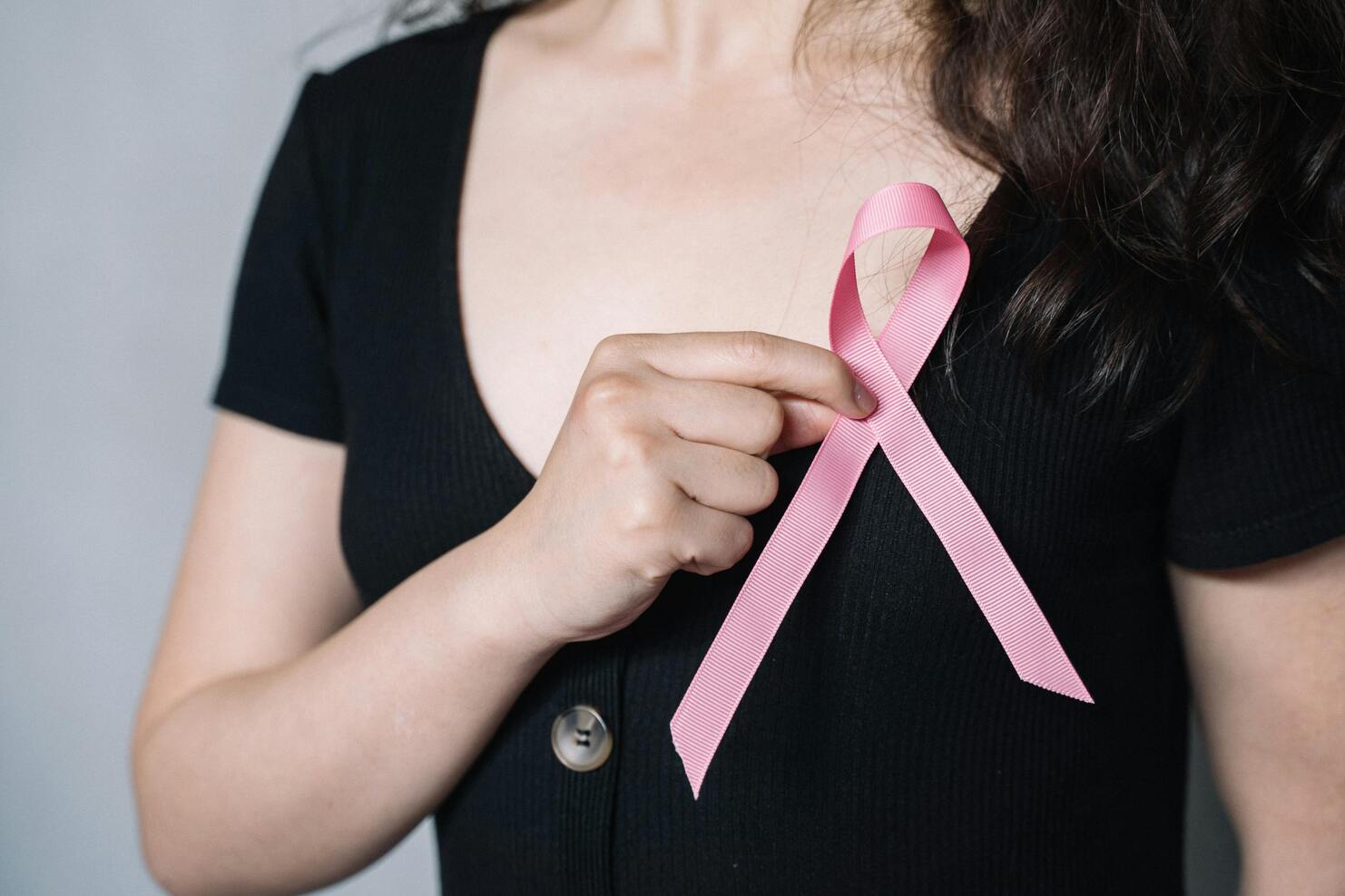 Nahaufnahme einer Person in schwarzer Kleidung, die ein rosa Bewusstseinsband mit der Hand hält.