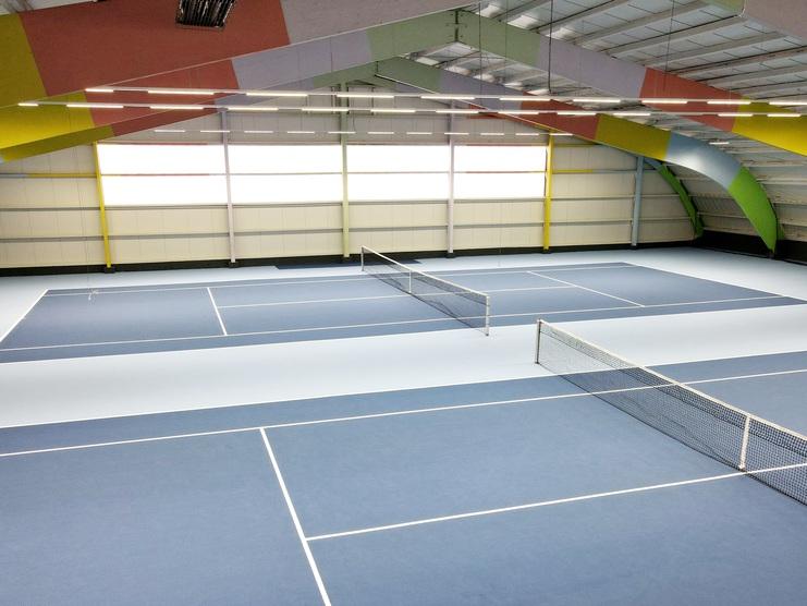Blick auf mehrere Tennisplätze in einer Halle mit blauen Spielflächen und bunten Wänden.