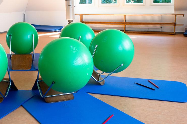 Fitnessraum mit grünen Gymnastikbällen auf blauen Matten, umgeben von Spiegeln und Fenstern.