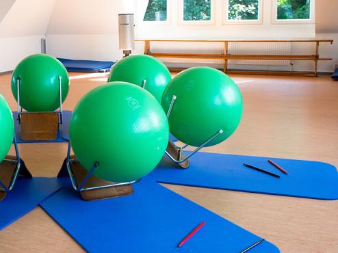 Fitnessraum mit grünen Gymnastikbällen auf blauen Matten, umgeben von Spiegeln und Fenstern.