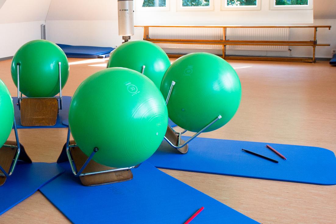 Fitnessraum mit grünen Gymnastikbällen auf blauen Matten, umgeben von Spiegeln und Fenstern.