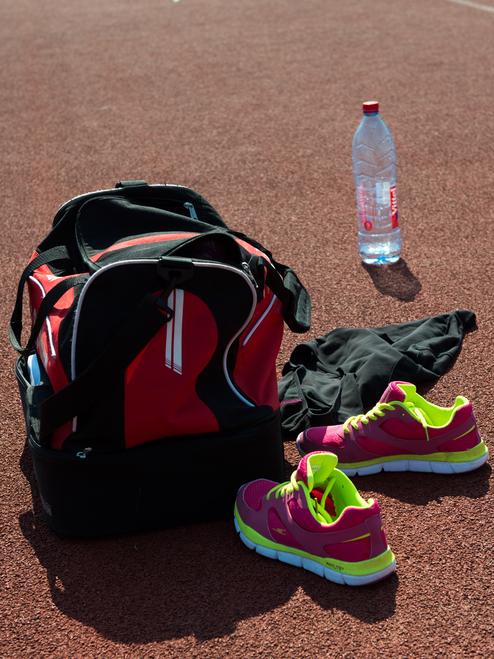 Sporttasche, pinke Sportschuhe, schwarze Kleidung und eine Wasserflasche auf einer orangefarbenen Laufbahn.
