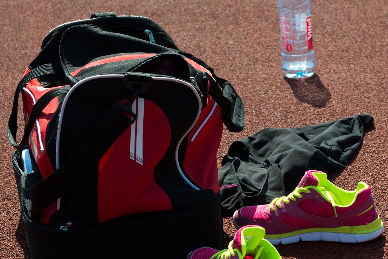 Sporttasche, pinke Sportschuhe, schwarze Kleidung und eine Wasserflasche auf einer orangefarbenen Laufbahn.