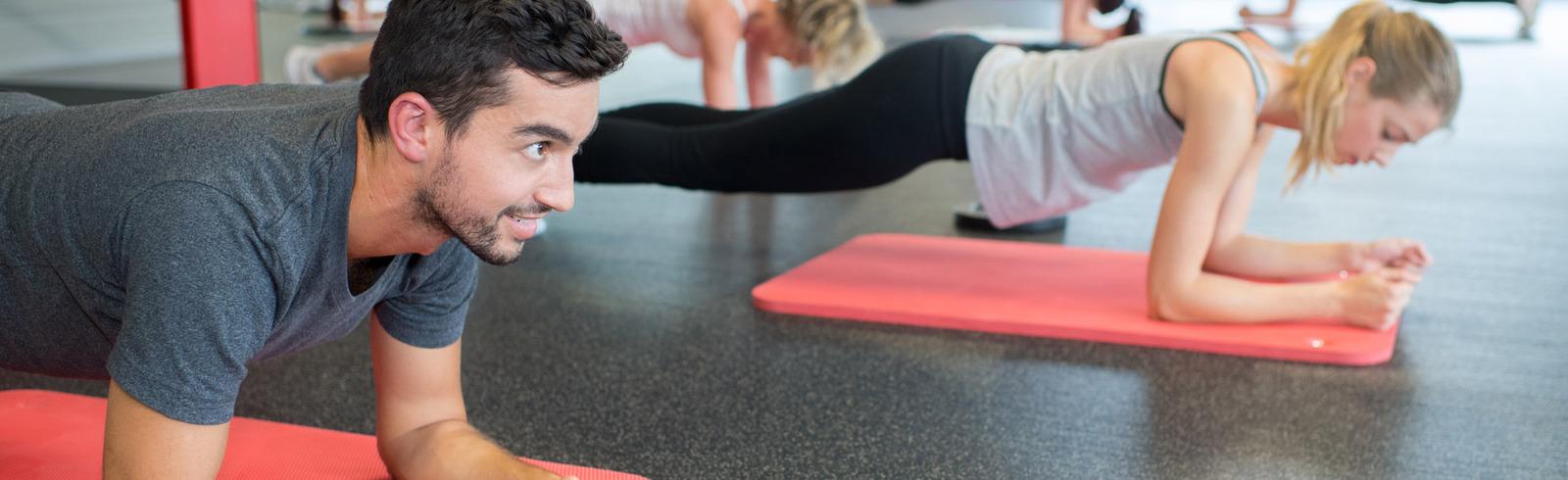 Mann und Frauen machen Plank-Übungen auf Yogamatten in einem Fitnessstudio. Helle, sportliche Atmosphäre.