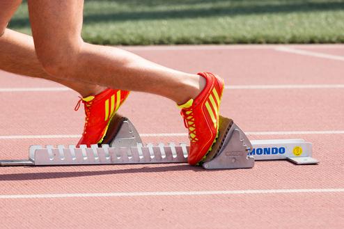 Nahaufnahme eines Fußes in einem roten Laufschuh, der auf einem Startblock auf einer Laufbahn steht.