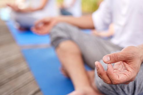 Nahaufnahme einer Hand, die im Meditationszustand auf einer blauen Yogamatte liegt, mit Fuß im Vordergrund.