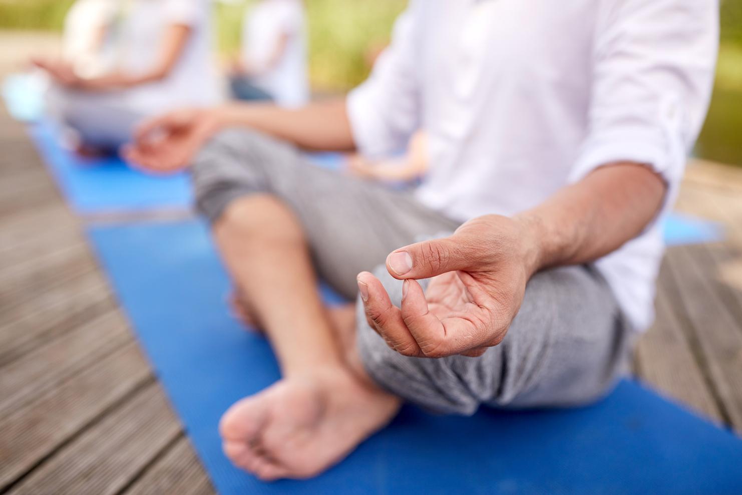 Nahaufnahme einer Hand, die im Meditationszustand auf einer blauen Yogamatte liegt, mit Fuß im Vordergrund.
