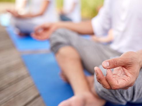 Nahaufnahme einer Hand, die im Meditationszustand auf einer blauen Yogamatte liegt, mit Fuß im Vordergrund.